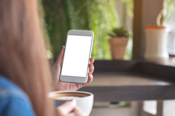 Mockup image of a woman holding and looking at a white smart phone with blank desktop screen while drinking coffee with blur green nature background