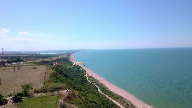 Aerial View. The paraglider flies over the coastline. The wing of the paraglider is blown by the wind. Row of sea and forest