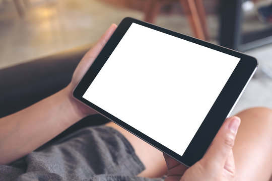 Mockup image of woman's hands holding black tablet pc with blank white desktop screen sitting in cafe