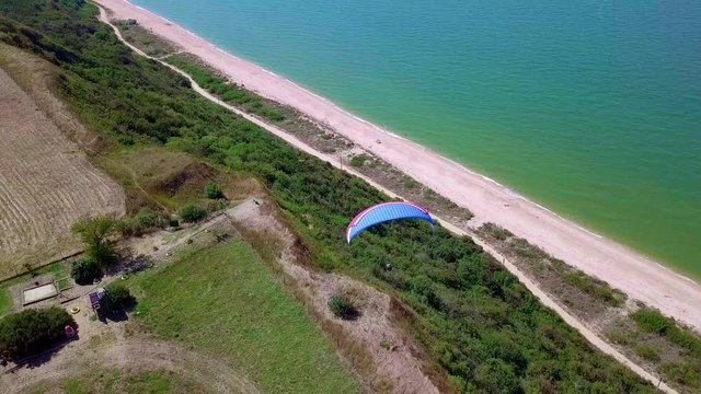 Aerial View. The paraglider flies over the coastline. The wing of the paraglider is blown by the wind. Row of sea and forest