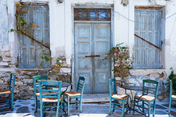 Blaue Türen an einem alten, verfallenen Gebäude mit griechischen Kafeneion Stühlen und Tischen...