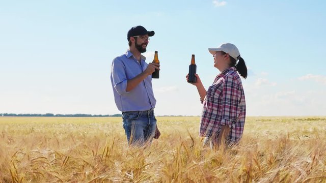 Two farmers drink beer from bottles standing in the middle of the barley field