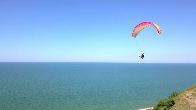 Aerial View. The paraglider flies over the coastline. The wing of the paraglider is blown by the wind. Row of sea and forest
