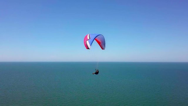 Aerial View. The paraglider flies over the coastline. The wing of the paraglider is blown by the wind. Row of sea and forest