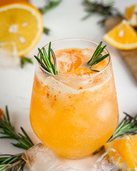 Orange cocktail with ice and rosemary in beautiful glass and jug with fresh ripe citrus on white background. Close up photography of sweet orange juice.
