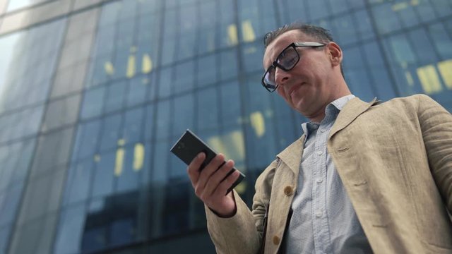 Man standing near modern office building and using smartphone