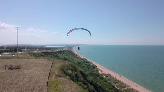 Aerial View. The paraglider flies over the coastline. The wing of the paraglider is blown by the wind. Row of sea and forest
