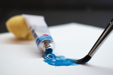 Blue oil paint, tube and brush on white paper, artistic concept