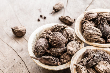 Whole black cardamom in coconut bowl on wooden background
