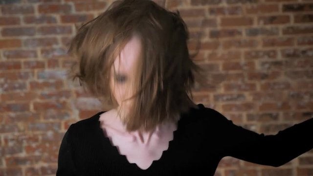 Young sexy girl with smoky eyes is dancing, shaking head, rock music, brick background