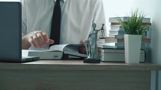 Lawyer reading law book in the office. Footage contains generic figurine of Lady Justice, a personification of moral force and it's origin is Justitia, goddess of Justice in Roman mythology