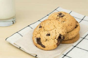close up of the chocolate chip cookies and a glass of milk at the wooden table.