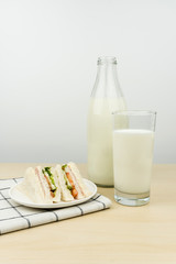 a glass of milk with milk bottle and the club sandwiches in a white round dish on the wooden table.