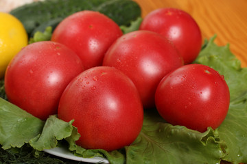 Group of six red ripe tomatoes with water drops lie on a lettuce leaves