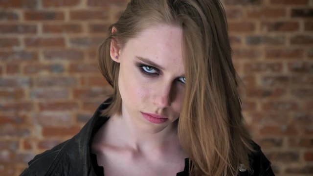 Young sexy confident girl with smoky eyes is watching at camera, brick background