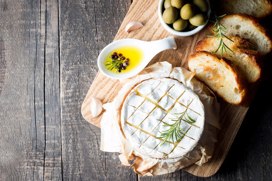 Baked camembert cheese. Fresh Brie cheese and a slice on a wooden board with nuts, honey, rosemary, baguette bread grilled toasts and leaves. Brie type of cheese. Italian, French cheese.