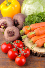 Many different vegetables include cabbage, tomatoes, peppers, carrots and beets on a wooden stand on a brown wooden background.