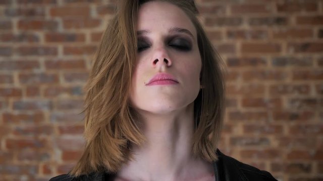 Young sexy serious girl with smoky eyes is watching at camera, close her eyes, brick background