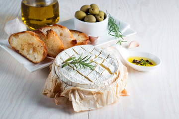 Baked camembert cheese. Fresh Brie cheese and a slice on a wooden board with nuts, honey, rosemary, baguette bread grilled toasts and leaves. Brie type of cheese. Italian, French cheese.