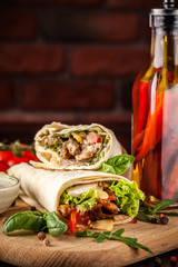 Mexican cuisine, burrito with chicken, cherry tomatoes, lettuce, mushrooms, rucola and chili peppers, on a black background. With salsa sauce. Copy space, selective focus