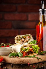 Mexican cuisine, burrito with chicken, cherry tomatoes, lettuce, mushrooms, rucola and chili peppers, on a black background. With salsa sauce. Copy space, selective focus