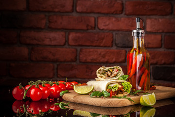 Mexican cuisine, burrito with chicken, cherry tomatoes, lettuce, mushrooms, rucola and chili peppers, on a black background. With salsa sauce. Copy space, selective focus