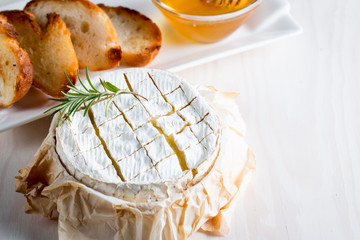 Baked camembert cheese. Fresh Brie cheese and a slice on a wooden board with nuts, honey, rosemary,...