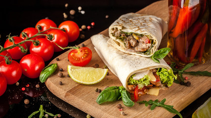 Mexican cuisine, burrito with chicken, cherry tomatoes, lettuce, mushrooms, rucola and chili peppers, on a black background. With salsa sauce. Copy space, selective focus