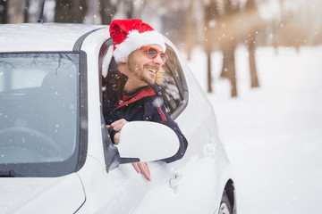 Man wearing Santa Claus hat and leaning on car window. Winter travel concept.