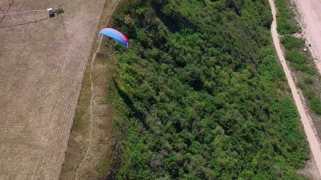 Aerial View. The paraglider flies over the coastline. The wing of the paraglider is blown by the wind. Row of sea and forest