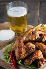 Close-up photo of bbq chicken wings with fries and beer. Barbeques meat with sauces, ketchup, mayonnaise. Fast and junk food concept. 