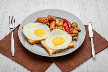Set for breakfast fried eggs, grilled vegetables, sausages. Bread on a wooden table.