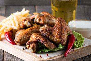 Close-up photo of bbq chicken wings with fries and beer. Barbeques meat with sauces, ketchup, mayonnaise. Fast and junk food concept. 