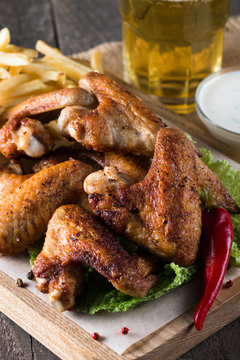 Close-up photo of bbq chicken wings with fries and beer. Barbeques meat with sauces, ketchup, mayonnaise. Fast and junk food concept. 