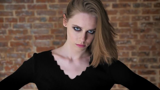 Young sext girl with smoky eyes is playing with hair, flirt concept, brick background