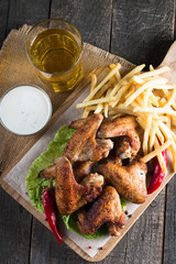 Close-up photo of bbq chicken wings with fries and beer. Barbeques meat with sauces, ketchup, mayonnaise. Fast and junk food concept. 