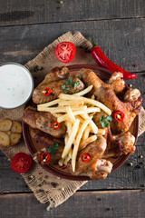 Close-up photo of bbq chicken wings with fries and beer. Barbeques meat with sauces, ketchup, mayonnaise. Fast and junk food concept. 