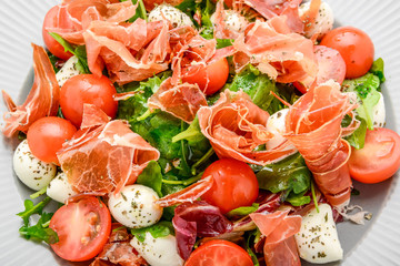 Salad with fresh vegetables with dried tomatoes, meat and mustard, mozzarella, prosciutto