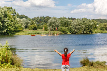 A girl with open arms, enjoys freedom outdoors in the middle of a natural landscape formed by a river and vegetation