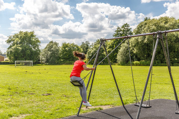 A girl takes a momentum on a swing in a playground on a sunny day