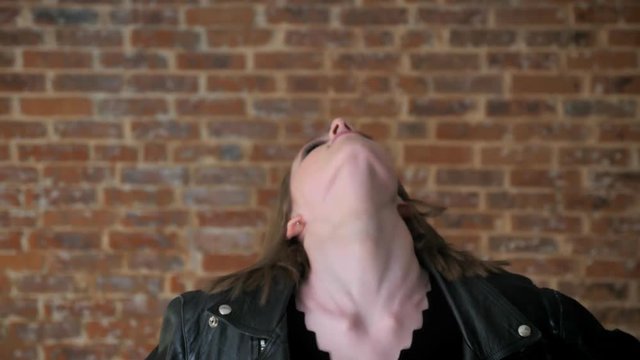 Young sexy girl with smoky eyes is dancing, shaking head, hardcore, brick background
