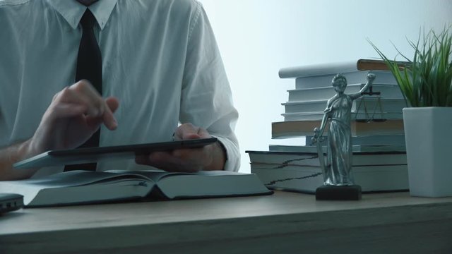 Lawyer using digital tablet computer in law firm office, focus on hands. Footage contains generic figurine of Lady Justice, personification of moral force and it's origin is Justitia