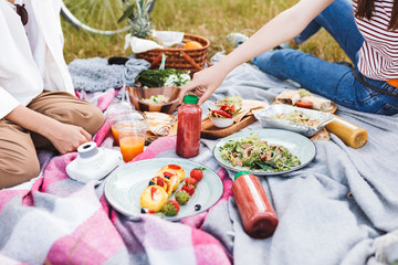 Close up photo of girls spending time on picnic with delicious food and drinks on blanket in city park