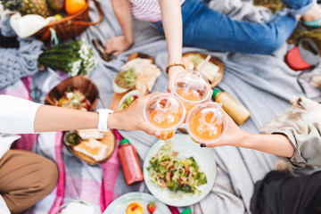 Close up girls holding cup to go with orange juice on beautiful picnic with variety of tasty food in city park © Anton