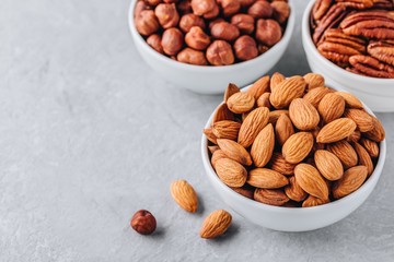 Almonds, pecans and hazelnuts in white bowls on grey background. Assortment of nuts.