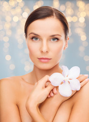 Obraz na płótnie Canvas wellness and beauty concept - beautiful bare woman with orchid flower over holidays lights background