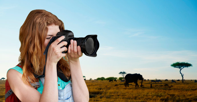 travel, tourism and photography concept - happy young woman with backpack and camera photographing over animals in african savannah background