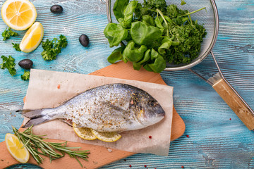 Fresh fish dorado top view. spinach and lemon healthy food spice on wooden board
