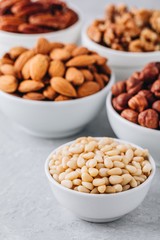 Pine nuts, almonds, pecans, walnuts and hazelnuts in white bowls on grey background. Mixed nuts.