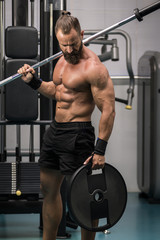 Naklejka premium Hombre fuerte con grandes músculos preparando peso para entrenar en el gimnasio. Ponerse en forma.